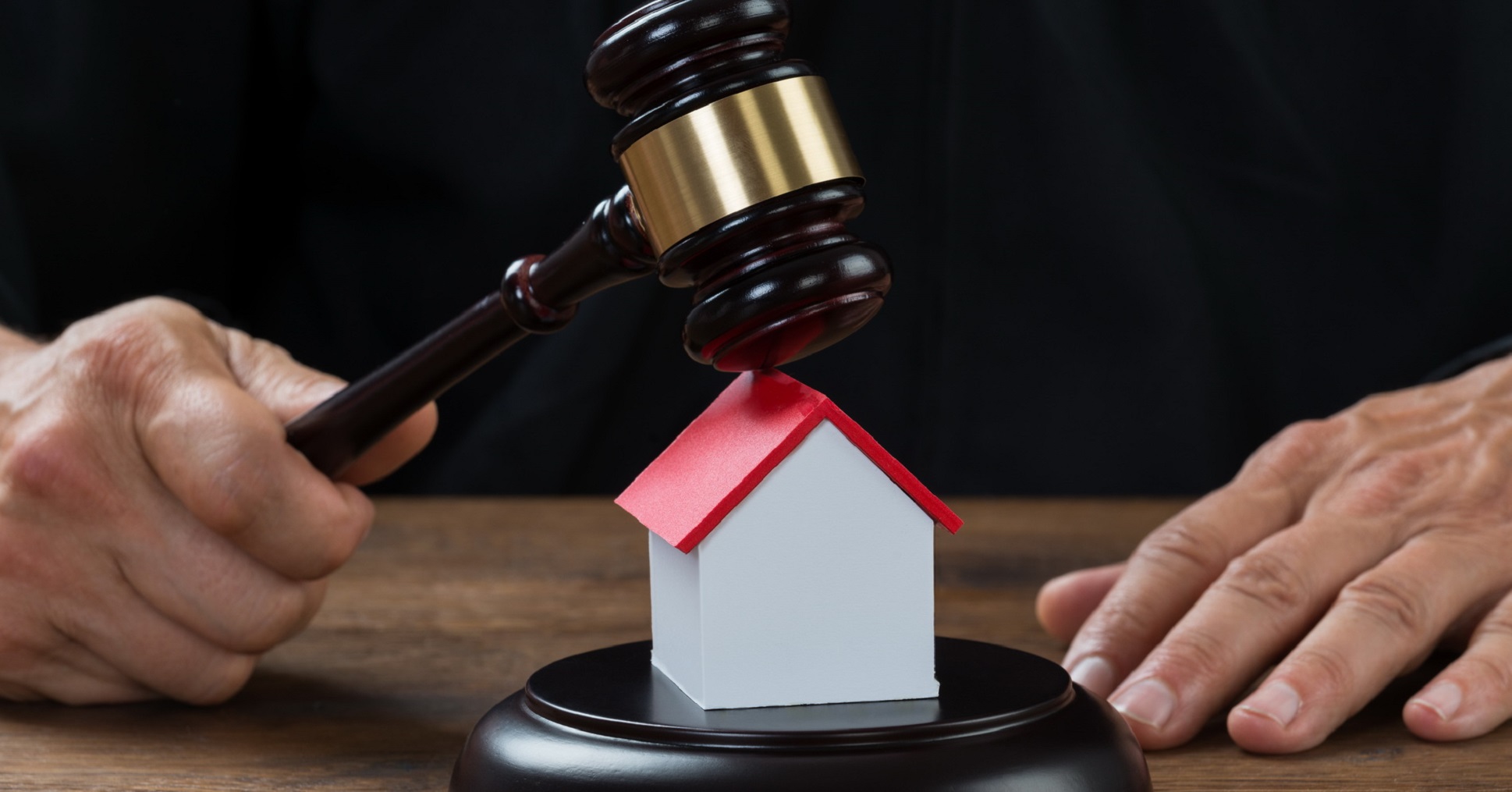 Judge Holding Gavel On House At Desk