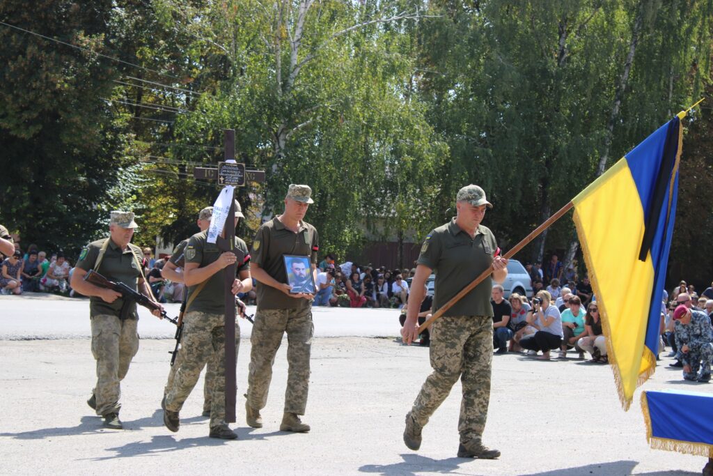 Військові несуть прапор, хрест та портрет загиблого воїна. Фото: Семенівська громада